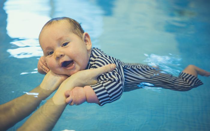 A young baby floating, supported by a parent's hands